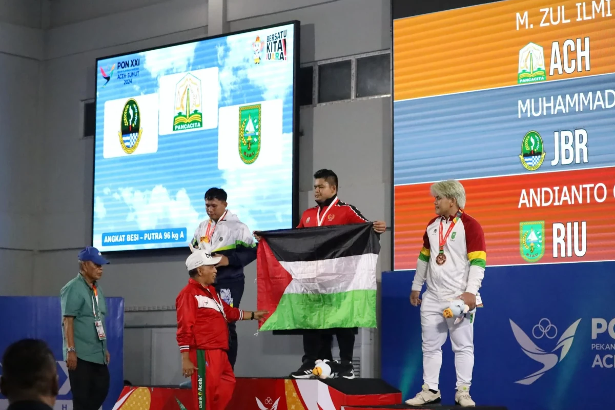 Lifter Aceh Zul Ilmi mengibarkan bendera Palestina usai memastikan kemenangan di kelas 96 kilogram putra. Foto: MC PON Aceh