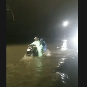 Warga menuntun sepeda motor melintas banjir di jalan rel, Pidie Jaya