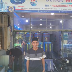 Muhammad Fajarul Aqsha pemilik depot air minum Sehat Water tersenyum di depan tokonya yang menyediakan program Infak Produktif air minum gratis bagi anak yatim piatu di Desa Kutablang, Lhokseumawe.