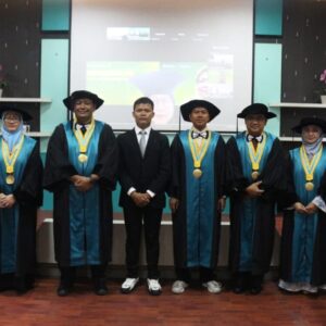 Dr. Andriy Anta Kacaribu mengenakan setelan jas hitam formal berdiri di tengah, didampingi oleh jajaran pimpinan, tim promotor, dan tim penguji Universitas Syiah Kuala yang mengenakan toga resmi pascasarjana usai Sidang Terbuka Promosi Doktor di Banda Aceh