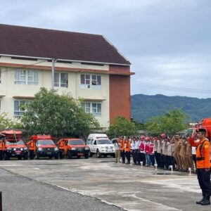 Pj Sekda Aceh Taufik dengan seragam dinas cokelat berdiri di atas podium memberikan penghormatan dalam Apel Kesiapsiagaan Bencana di Lapangan Gudang BPBA.