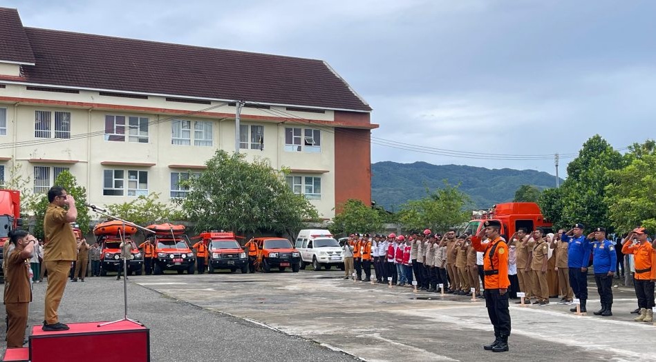 Pj Sekda Aceh Taufik dengan seragam dinas cokelat berdiri di atas podium memberikan penghormatan dalam Apel Kesiapsiagaan Bencana di Lapangan Gudang BPBA.