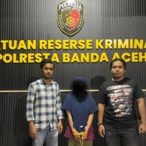 foto tersangka perempuan dengan tangan terikat tali kuning di depan logo Polresta Banda Aceh.
