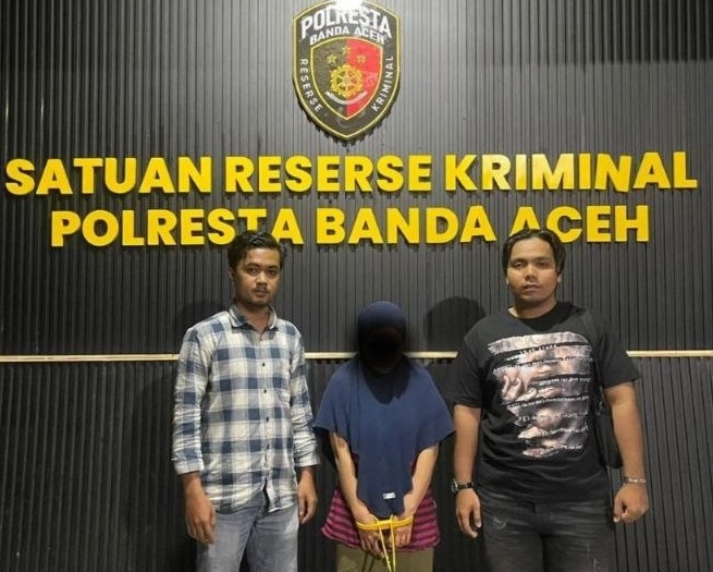 foto tersangka perempuan dengan tangan terikat tali kuning di depan logo Polresta Banda Aceh.