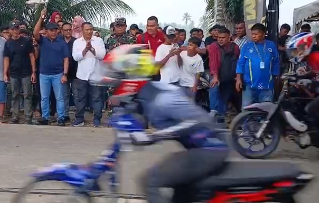 Dandim 0103 Aceh Utara Letkol Inf Faisal mengenakan kaos berkerah warna biru dongker mengangkat bendera start bermotif papan catur untuk melepas dua pembalap drag bike yang melesat cepat di lintasan balap Tanah Luas.