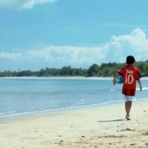 Poster resmi atau cuplikan adegan film Forza yang menampilkan Bima, anak laki-laki asal Bali bersanding bersama mantan pemain legendaris AC Milan dengan latar belakang lapangan sepak bola.