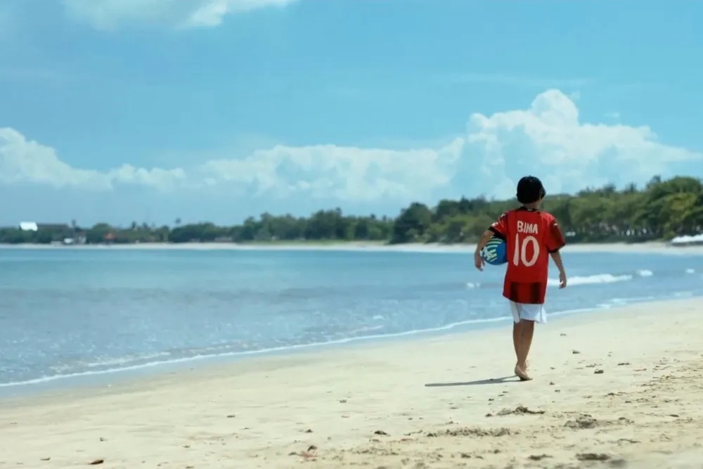 Poster resmi atau cuplikan adegan film Forza yang menampilkan Bima, anak laki-laki asal Bali bersanding bersama mantan pemain legendaris AC Milan dengan latar belakang lapangan sepak bola.