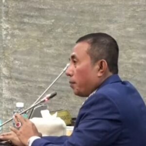 Anggota DPRA Irfannusir Rasma memakai jas biru berbicara melalui mikrofon saat melakukan interupsi dalam rapat paripurna.