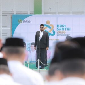 Kepala Kantor Kementerian Agama Aceh Besar, Saifuddin atau Yahwa, sedang memberikan amanat di atas mimbar upacara Hari Santri Nasional 2026 dengan latar belakang baliho bertuliskan Hari Santri 2026