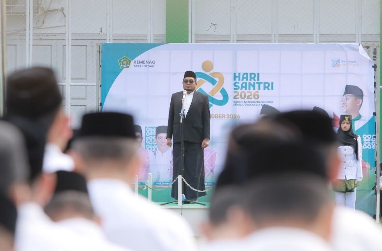 Kepala Kantor Kementerian Agama Aceh Besar, Saifuddin atau Yahwa, sedang memberikan amanat di atas mimbar upacara Hari Santri Nasional 2026 dengan latar belakang baliho bertuliskan Hari Santri 2026