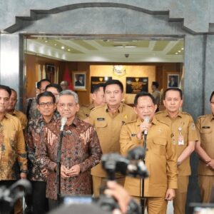 Mendagri Muhammad Tito Karnavian memegang mikrofon saat memberikan keterangan pers bersama jajaran pejabat Kemendagri dan Kemenkeu di depan pintu masuk utama berarsitektur batu alam abu-abu.