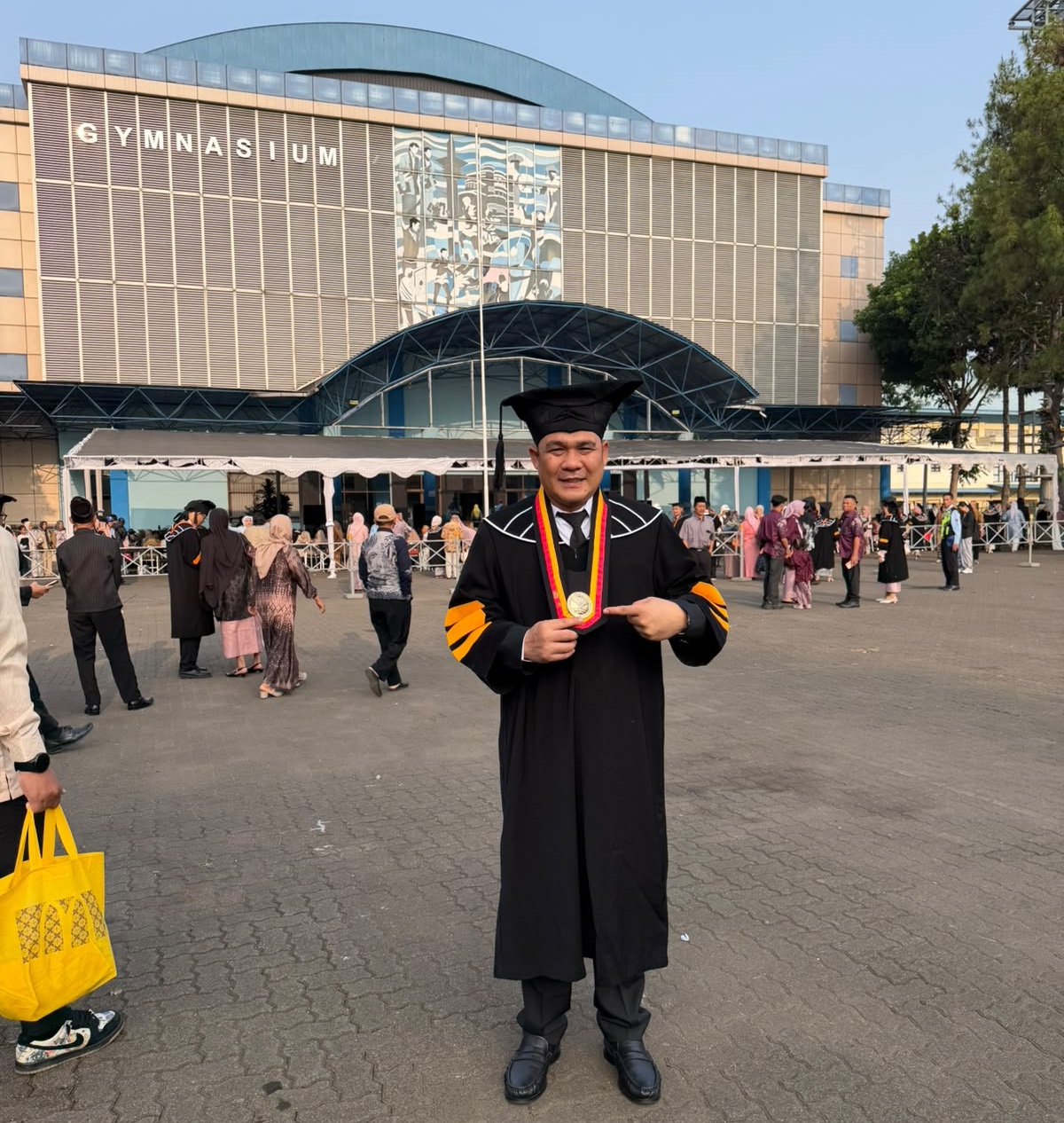 Kepala Cabang Dinas Pendidikan Wilayah Kabupaten Aceh Utara, Dr. Muhammad Johan, S.Pd., M.Pd., mengenakan toga wisuda program doktor di depan Gedung Gymnasium Universitas Pendidikan Indonesia (UPI) Bandung