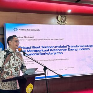 Dirjen Risbang Kemdiktisaintek Dr Fauzan Adziman memakai baju batik cokelat sedang berpidato di podium Aula PNL dengan latar belakang layar persentase digital