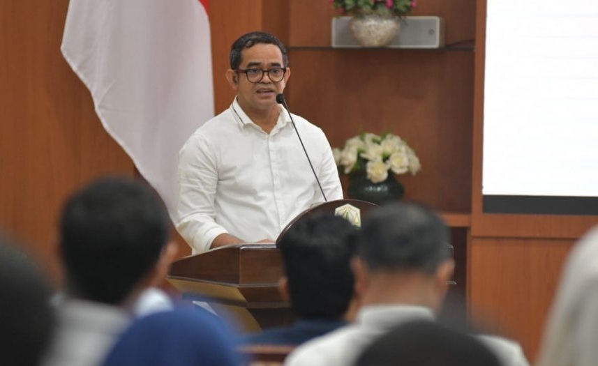 Pj. Sekda Aceh Taufik mengenakan kemeja putih dan kacamata saat menyampaikan kata sambutan di balik podium kayu dalam acara peluncuran program kemitraan demokrasi.