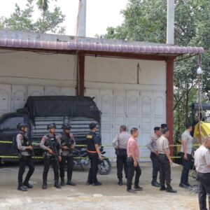 Aparat kepolisian bersenjata lengkap dan rompi antipeluru berjaga di depan dua ruko putih yang telah dipasangi garis polisi warna kuning di Gampong Beureueh Dua, Kecamatan Mutiara Timur, Pidie. Tampak sebuah mobil pikap hitam terparkir di depan ruko