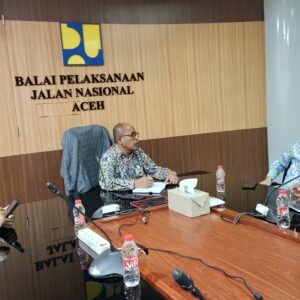 Wali Kota Lhokseumawe Sayuti Abubakar memakai kemeja batik biru muda duduk berdiskusi dalam rapat koordinasi di dalam kantor BPJN Aceh