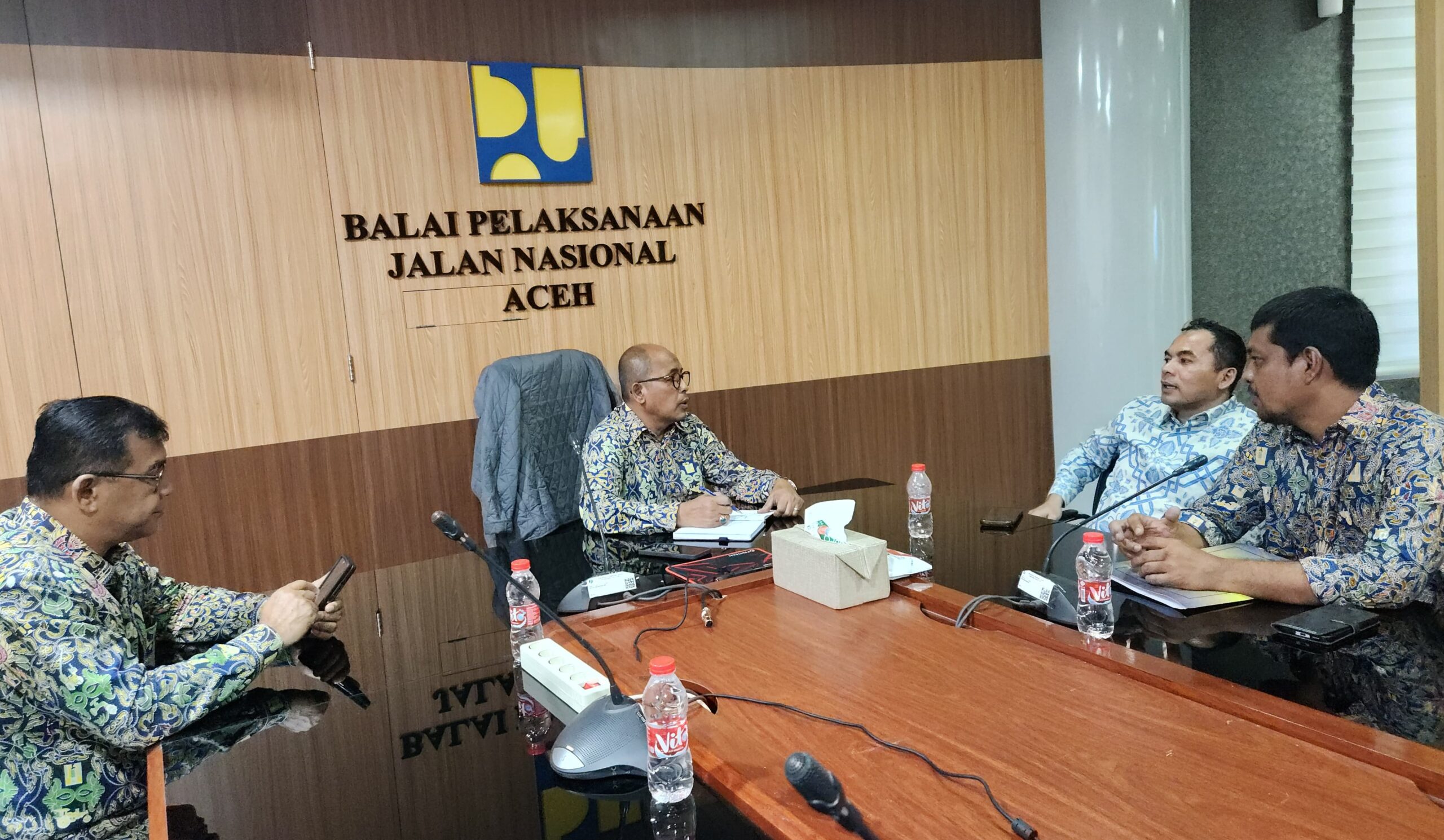 Wali Kota Lhokseumawe Sayuti Abubakar memakai kemeja batik biru muda duduk berdiskusi dalam rapat koordinasi di dalam kantor BPJN Aceh