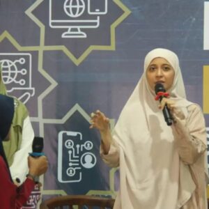 Kepala Pusat Pengembangan Literasi Digital Komdigi Rizki Ameliah mengenakan jilbab krem krem sedang berbicara menggunakan mikrofon di acara literasi digital KPRK MUI di Depok