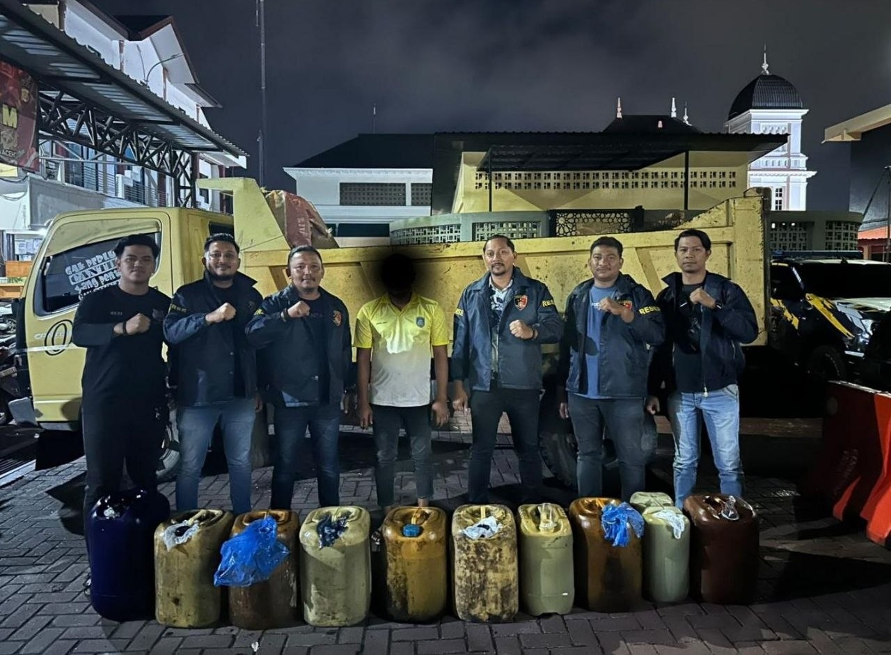 Sejumlah personel Satreskrim Polresta Banda Aceh berfoto bersama seorang pria berkaus kuning di depan dump truck, dengan deretan jerigen solar berjajar di bagian depan.